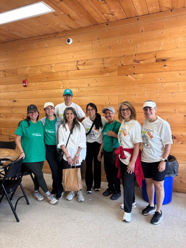A group of volunteers posing together in a wood-paneled room, wearing green volunteer shirts and white Green Team shirts.